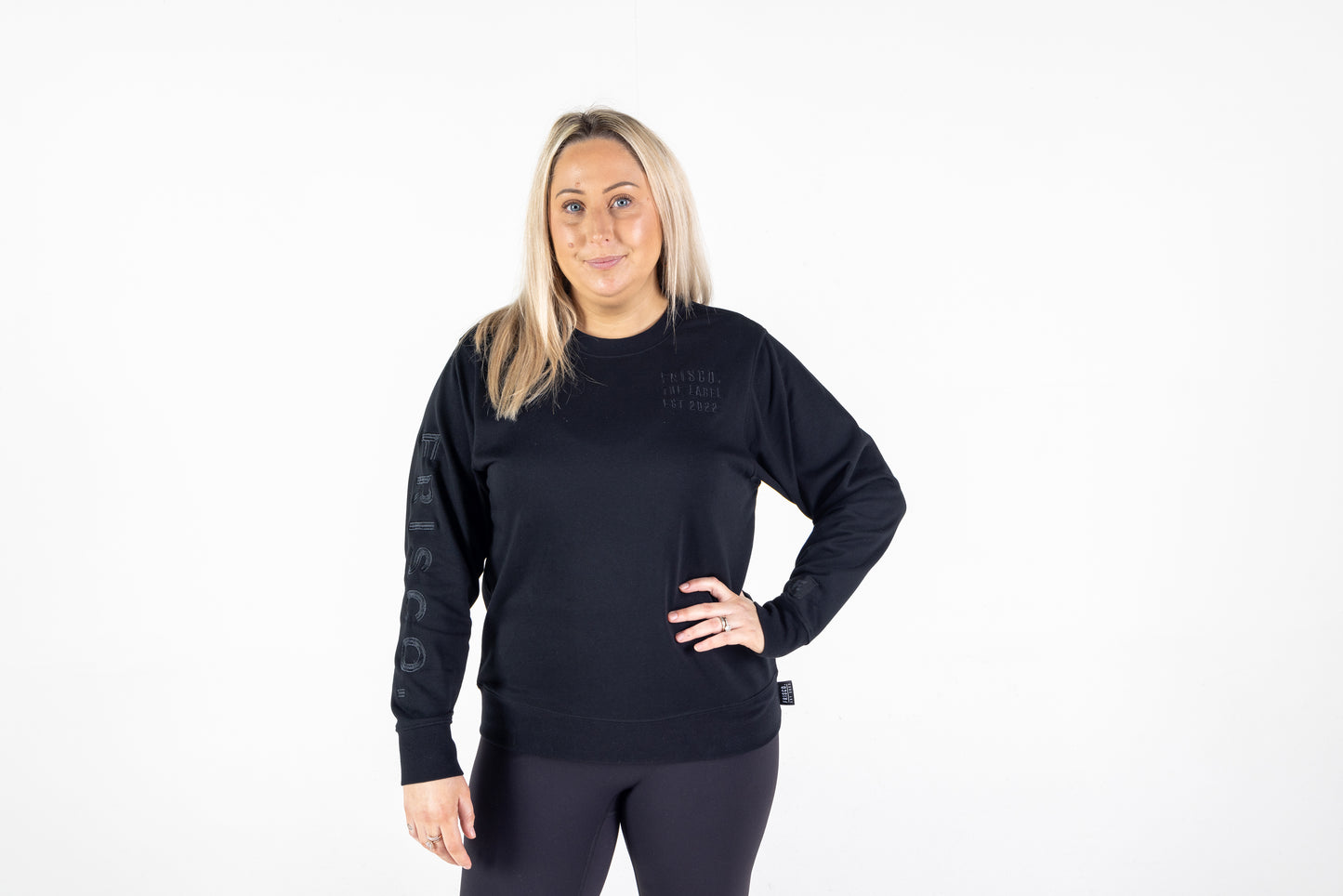 Frisco Women's activewear XL longsleeve crew top in black with black embroidery, shown from front, model hand on left hip