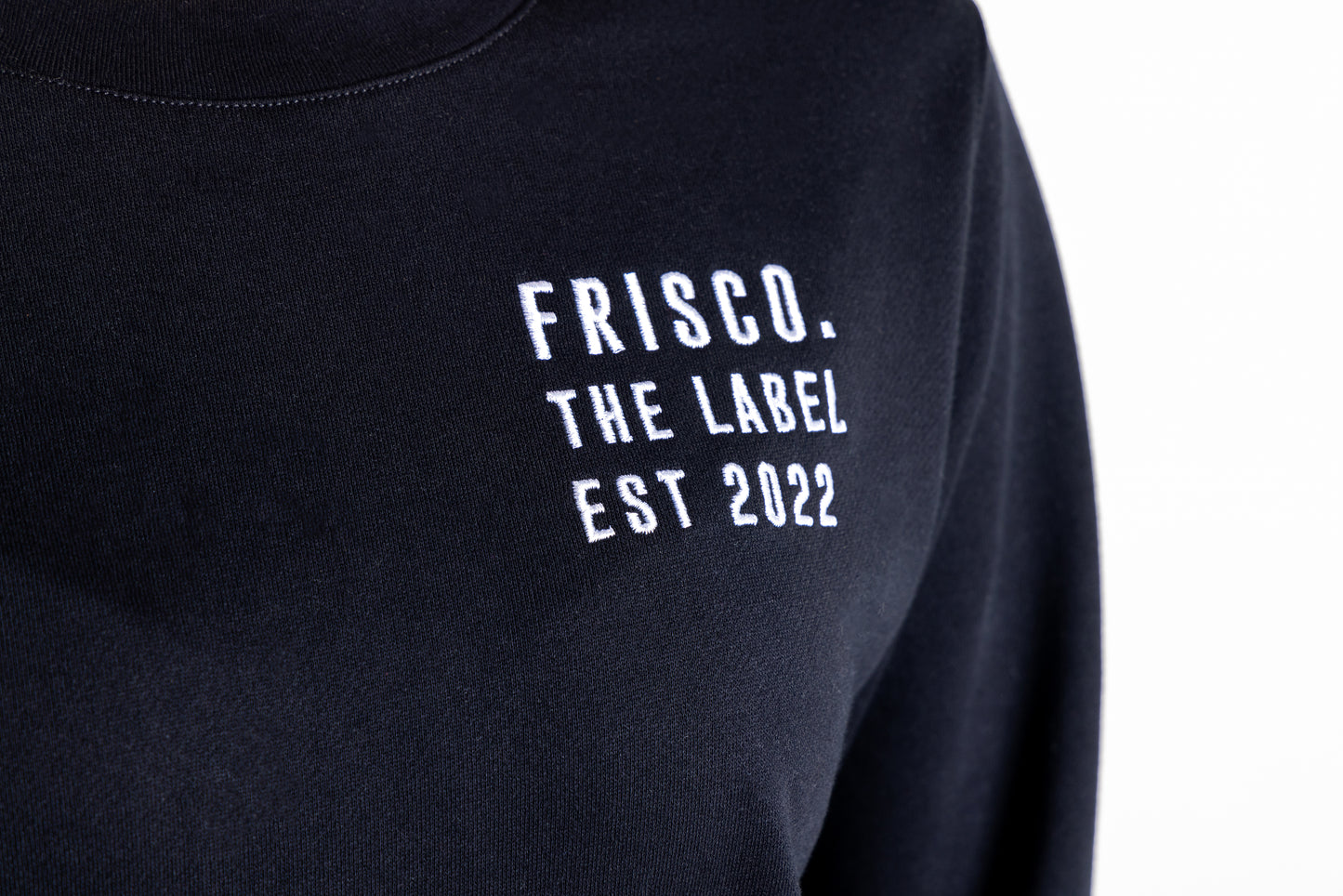 "Frisco Women's activewear small longsleeve crew top in black, extreme closeup of white embroidery on chest that says Frisco, the label, est 2022 "