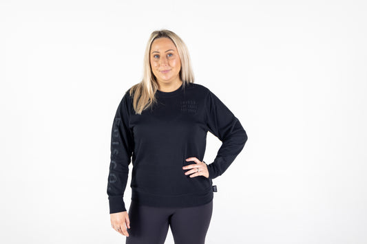 Frisco Women's activewear XL longsleeve crew top in black with black embroidery, shown from front, model hand on left hip 