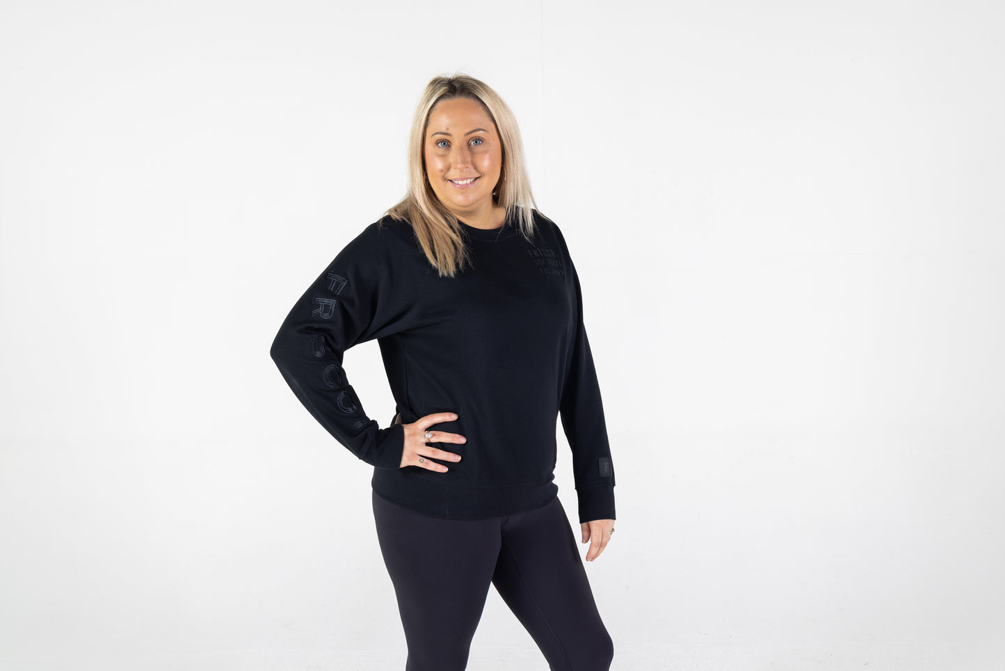 Frisco Women's activewear XL longsleeve crew top in black with black embroidery, shown from front, model hand on right hip 