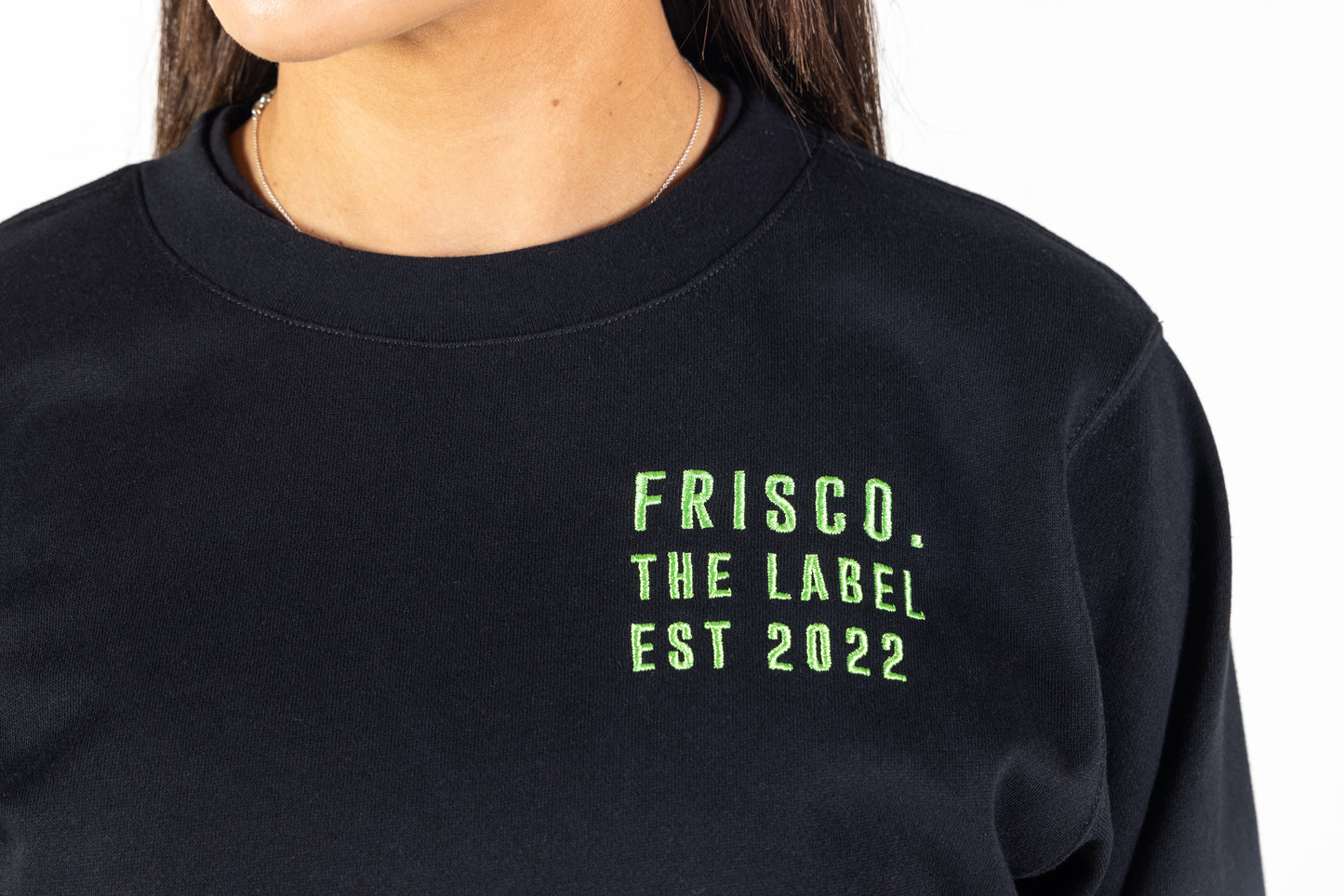 "Frisco Women's activewear small longsleeve crew top in black, closeup of green embroidery on chest that says Frisco, the label, est 2022 "