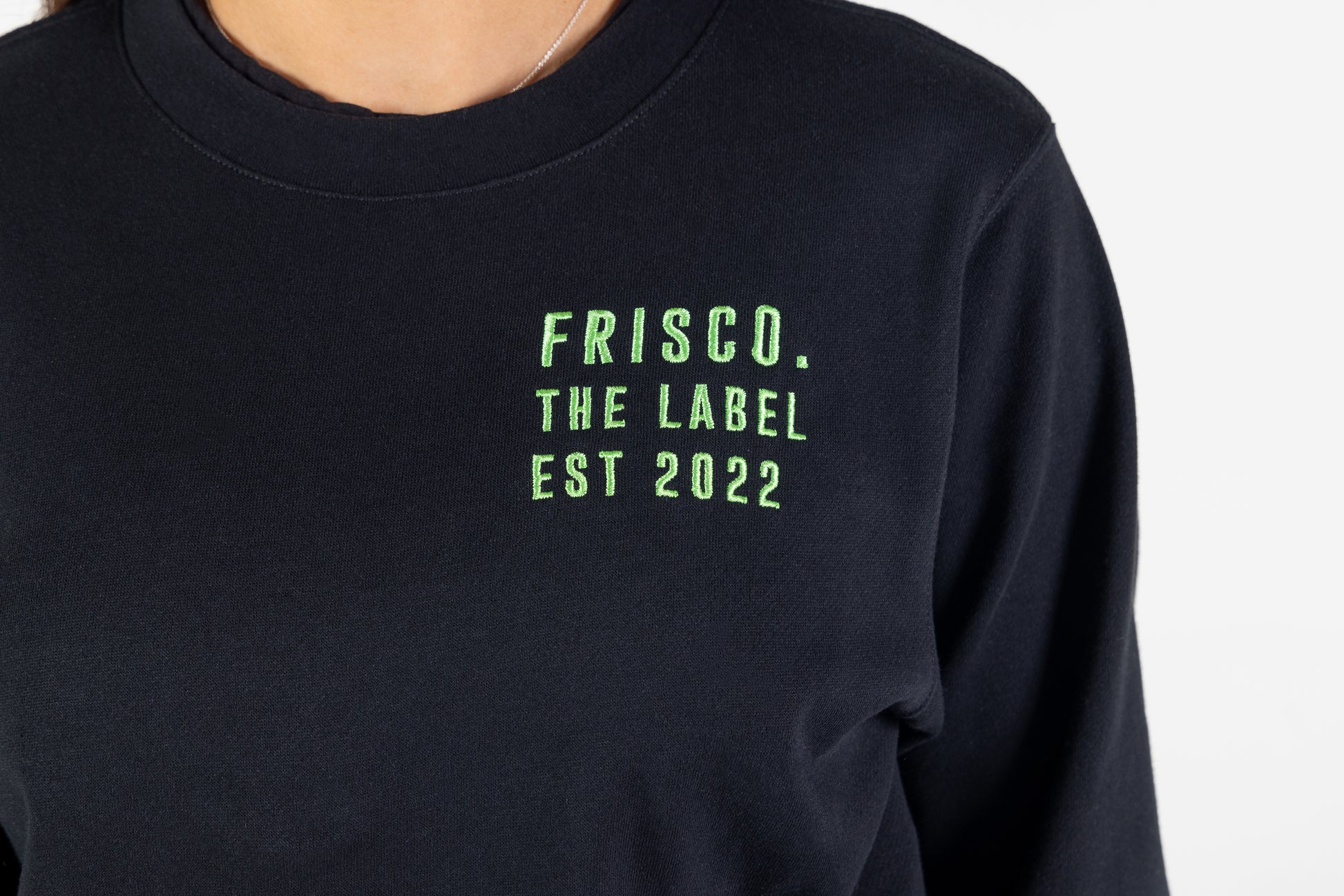 "Frisco Women's activewear small longsleeve crew top in black, closeup of green embroidery on chest that says Frisco, the label, est 2022 "