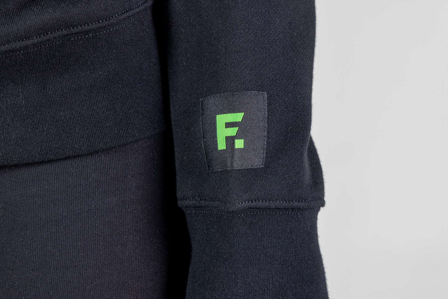 "Frisco Women's activewear small longsleeve crew top in black, extreme closeup of sleeve patch with green Frisco logo "