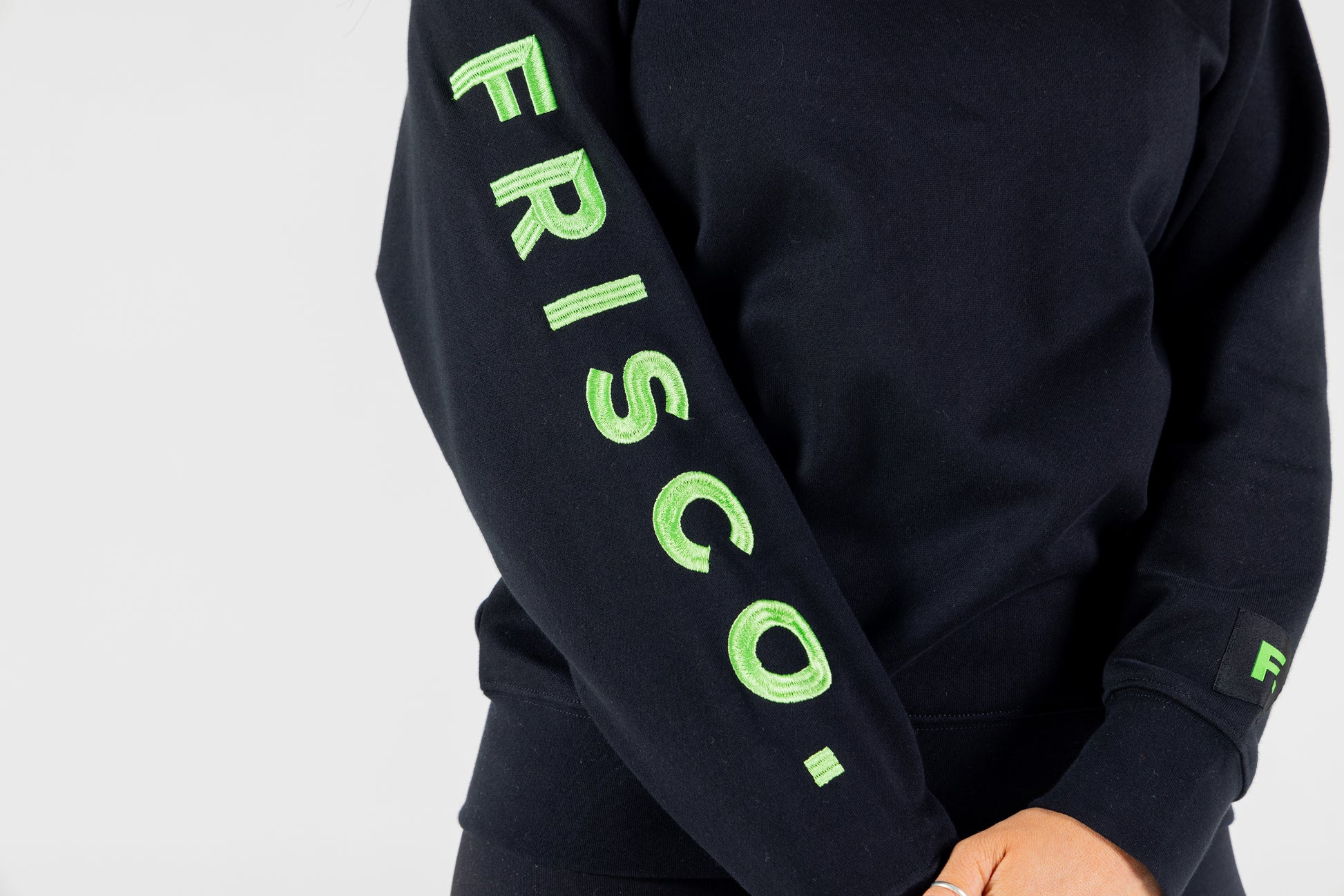 "Frisco Women's activewear small longsleeve crew top in black, closeup of right sleeve green embroidery that says Frisco. "