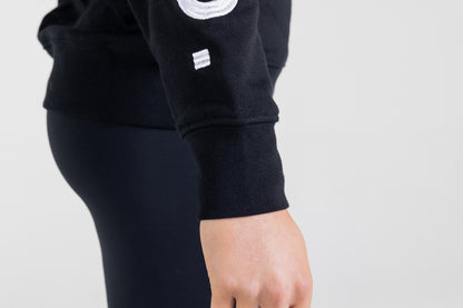 "Frisco Women's activewear small longsleeve crew top in black, extreme closeup of right sleeve cuff showing white embroidery that says Frisco. "